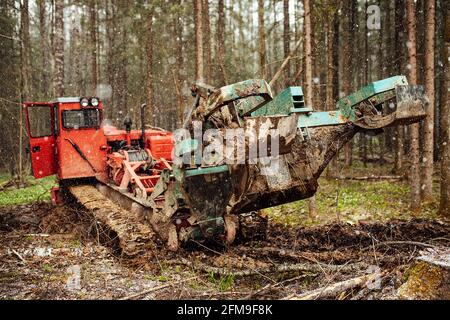 Ein Raupentraktor fährt durch eine Waldlichtung. Ein industrieller Bulldozer steckt im Schlamm fest. Lastwagen laufen im Boden Stockfoto