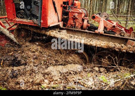 Ein Raupentraktor fährt durch eine Waldlichtung. Ein industrieller Bulldozer steckt im Schlamm fest. Lastwagen laufen im Boden Stockfoto