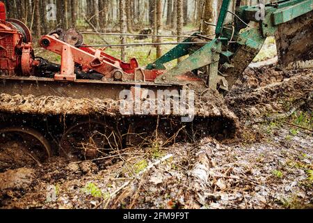 Ein Raupentraktor fährt durch eine Waldlichtung. Ein industrieller Bulldozer steckt im Schlamm fest. Lastwagen laufen im Boden Stockfoto