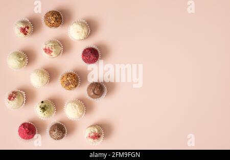 Verschiedene Bonbons mit Schokolade, Karkade, Kokosnuss und Nüssen auf einem pastellrosa Hintergrund. Trüffel oder Energiebälle. Platz zum Kopieren, Draufsicht, flach liegend. Stockfoto