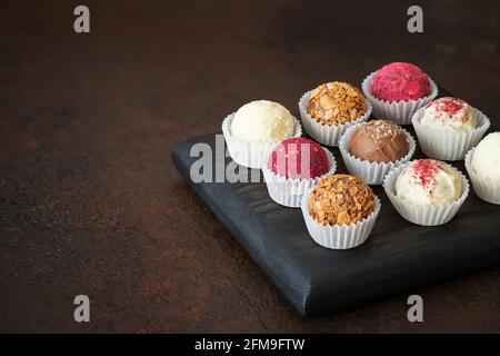 Schokolade, Obst und Nusstrüffel auf dunkelbraunem Hintergrund. Hausgemachte Süßigkeiten oder Energiekugeln. Speicherplatz kopieren. Stockfoto