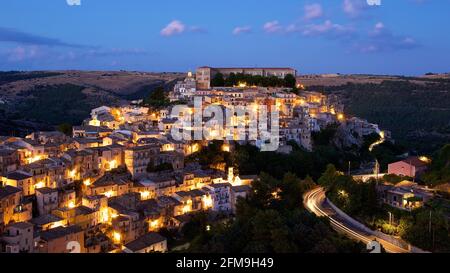 Italien, Sizilien, Südostsizilien, Barockwinkel, Ragusa, Abendaufnahme, Blick auf Ragusa Ibla, beleuchtet von warmem Straßenlicht, die Chiesa Anime Sante del Purgatorio befindet sich links unten, das Castello Vecchio befindet sich rechts oben auf dem Hügel, blauer Abendhimmel mit einigen grau-weißen Wolken Stockfoto