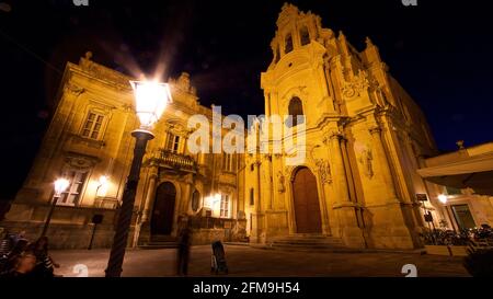 Italien, Sizilien, Südost-Sizilien, Barockwinkel, Ragusa, Ragusa bei Nacht, beleuchtete Kirche Chiesa di San Giuseppe, extreme Weitwinkelansicht von schräg unten, im Vordergrund links eine glitzernde helle Straßenlampe, wenige verschwommene Menschen Stockfoto