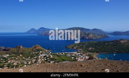 Italien, Sizilien, Äolische Inseln, Vulcano, Gipfel des Vulkankrater, Blick vom Krater auf Vulcano, Lipari und Salina, tiefblauer wolkenloser Himmel, Lavasteine im Vordergrund Stockfoto