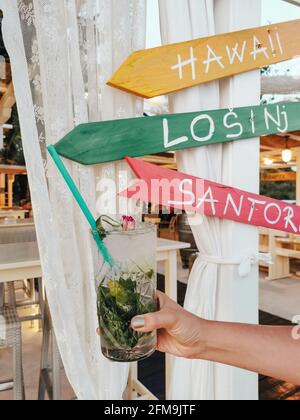 Frauenhand mit Mojito-Cocktail vor einem bunten Schild in der Strandbar. Stockfoto