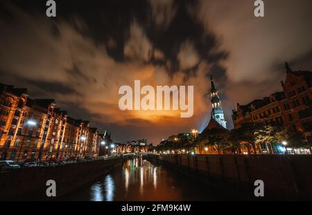 Speicherstadt Hamburg bei Nacht mit Blick von der Brücke zur Katharinenkirche und zur Elbphilharmonie. Stadtbild bei Nacht. Lichter Reflexion auf dem Wasser und Himmel. Stockfoto