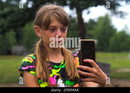 Unschärfe überrascht zehn Jahre altes Mädchen finden etwas auf dem Smartphone. Schöne Teenager-Mädchen nimmt Selfie, während allein auf dem Park stehen. Blogging und Live Stockfoto