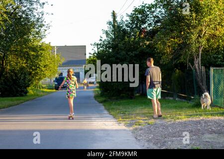 Unschärfe glücklich junge Mädchen spielen auf dem Skateboard auf der Straße. Mann, der mit Hund auf dem Hintergrund läuft. Kaukasische Kind Reiten Penny Board, üben Skateboarding Stockfoto