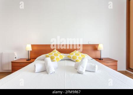 Hotelzimmer mit großem Bett, mit ein paar Handtüchern und Kissen darauf. Auf jeder Seite befinden sich Nachttische mit Lampen. Stockfoto