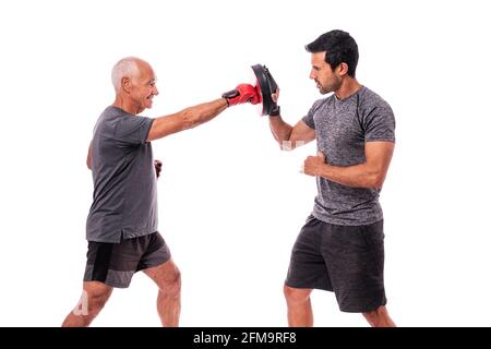 Älterer männlicher Athlet in hervorragender körperlicher Verfassung, in Boxhandschuhen, mit einem Fitnesstrainer, beim Boxen üben. Auf einem weißen, isolierten Hintergrund. Stockfoto