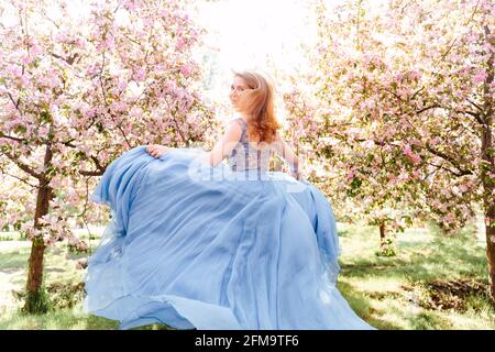 Eine rothaarige Frau in einem blauen Seidenkleid läuft durch den Garten. Stockfoto