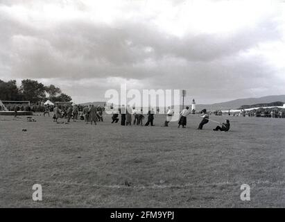 1956, historisch, draußen auf einem Grasfeld, bei einem Hochlandspiel, einige Männer, einige in Anzügen und einige in Kilts, möglicherweise Zuschauer, die an einem freundlichen 'Tauziehen'-Wettbewerb teilnehmen, Schottland, Großbritannien. Stockfoto