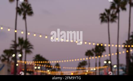 Defokussierte beleuchtete elektrische Girlande, Palmen Silhouetten, Oceanside California USA. Ozeanstrand tropisch rosa Sonnenuntergang, pazifikküste lila Dämmerungshimmel. Stimmung in Los Angeles. Glühlampe leuchtet. Stockfoto