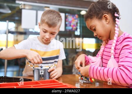 Baukasten für eine Gruppe von multirassischen Kindern, die Spielzeug erstellen. Nahaufnahme von konzentriertem afrikanischem Mädchen und kaukasischem Jungen, die am Projekt arbeiten und positive Emotionen haben. Konzept der Wissenschaftsingenieurwesen. Stockfoto