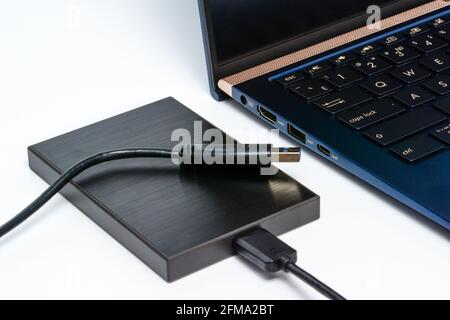Externe Festplatte, die über ein usb 3.0-Kabel mit dem Laptop verbunden ist. Konzept der Datenspeicherung auf einer tragbaren festplatte. Nahaufnahme auf weißer Oberfläche mit Schatten. Stockfoto