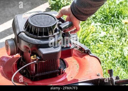 Nahaufnahme der Hand des kaukasischen Mannes, die einen roten Rasenmäher ansaugend. Vorbereitung zum Mähen des Hinterhofrasen. Stockfoto
