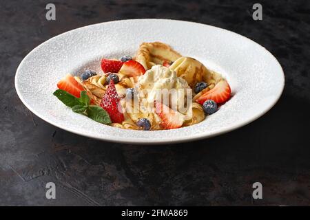 Köstliche dünne Pfannkuchen mit Erdbeeren, Quark und Honig auf schwarzem Tisch, Draufsicht, Kopierplatz Stockfoto