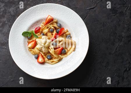 Köstliche dünne Pfannkuchen mit Erdbeeren, Quark und Honig auf schwarzem Tisch, Draufsicht, Kopierplatz Stockfoto