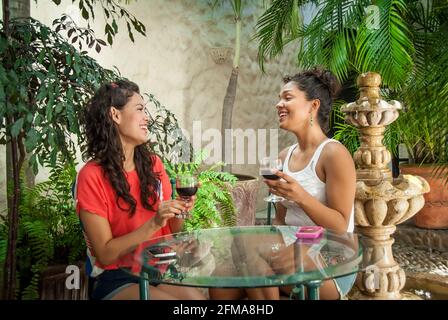 Zwei lachende junge hispanische Frauen auf einer tropischen Terrasse mit Rotwein - Casa Amorita B&B, Puerto Vallarta, Jalisco, Mexiko. #613 PV Stockfoto