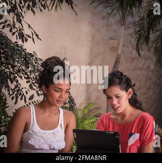 2 junge hispanische Frauen nutzen einen Laptop auf der tropischen Terrasse des Casa Amorita B&B, Puerto Vallarta, Bahia de Banderas, Jalisco, Mexiko. #613 PV Stockfoto