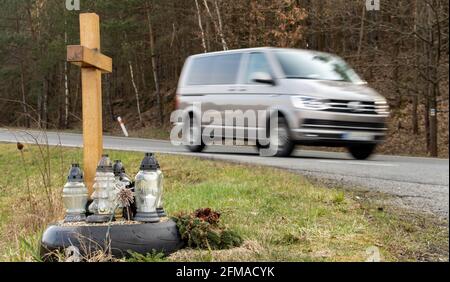 Ein Gedenkkreuz am Straßenrand mit Kerzen zum Gedenken an den tragischen Tod, auf einer Fahrt im Hintergrund verschwommenes Auto. Stockfoto