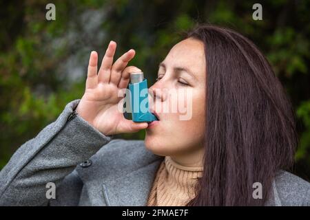 Hübsche junge Brünette Frau mit einem Asthma-Inhalator während starker Asthmaanfall wird pharmazeutisches Produkt verwendet, um Keuchen zu verhindern und zu behandeln und Stockfoto