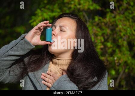 Hübsche junge Brünette Frau, die Asthma-Inhalator während starker Asthmaanfall verwendet, wird pharmazeutisches Produkt verwendet, um Keuchen zu verhindern und zu behandeln und Stockfoto