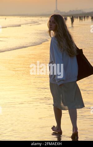 Eine teilweise silhouettierte Form einer Frau, die bei Ebbe barfuß in der Brandung läuft, Brighton & Hove, Sussex, England, Großbritannien Stockfoto