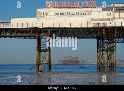 Der verfallene West Pier von Brighton wurde in die Struktur des „Brighton Pier“, des Palace Pier, eingefasst. Mann beim Joggen am Ufer im Vordergrund. Stockfoto