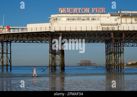 Der verfallene West Pier von Brighton wurde in die Struktur des „Brighton Pier“, des Palace Pier, eingefasst. Mann geht schwimmen. Stockfoto