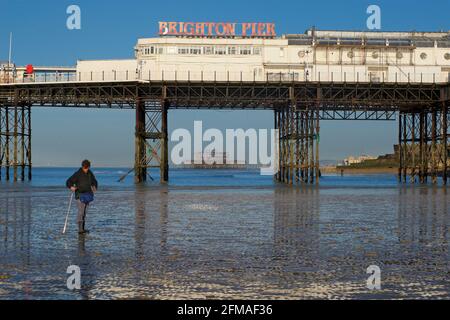 Der verfallene West Pier von Brighton wurde in die Struktur des „Brighton Pier“, des Palace Pier, eingefasst. Fischer sammeln Ragworm für Köder im Vordergrund. Stockfoto