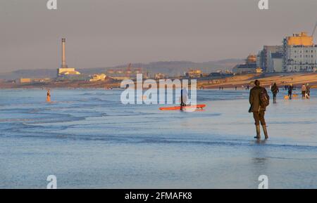 Leute, die bei Ebbe am frühen Morgen am Strand spazieren gehen. Brighton & Hove, Sussex, England, Großbritannien. Blick nach Westen in Richtung Shoreham, dem Kraftwerk in der Ferne. Stockfoto