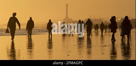 Brighton und Hove Beach bei Ebbe mit Blick nach Westen in Richtung Shoreham. Silhouetten von Menschen, die bei Sonnenuntergang am Sandstrand entlang wandern. East Sussex, England Stockfoto