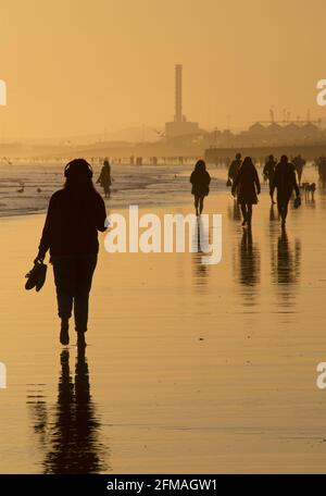 Brighton und Hove Beach bei Ebbe mit Blick nach Westen in Richtung Shoreham. Silhouetten von Menschen, die bei Sonnenuntergang am Sandstrand entlang wandern. East Sussex, England Stockfoto