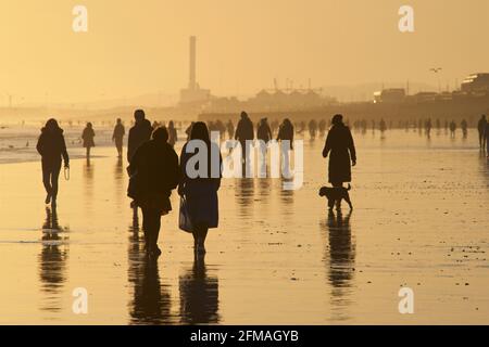 Brighton und Hove Beach bei Ebbe mit Blick nach Westen in Richtung Shoreham. Silhouetten von Menschen, die bei Sonnenuntergang am Sandstrand entlang wandern. East Sussex, England Stockfoto