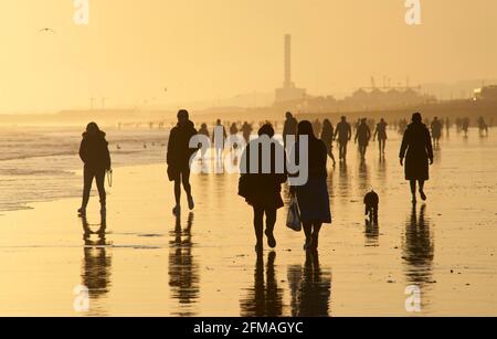 Brighton und Hove Beach bei Ebbe mit Blick nach Westen in Richtung Shoreham. Silhouetten von Menschen, die bei Sonnenuntergang am Sandstrand entlang wandern. East Sussex, England Stockfoto