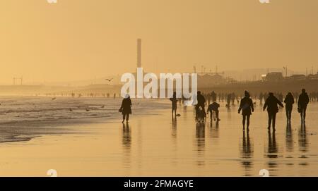 Brighton und Hove Beach bei Ebbe mit Blick nach Westen in Richtung Shoreham. Silhouetten von Menschen, die bei Sonnenuntergang am Sandstrand entlang wandern. East Sussex, England Stockfoto
