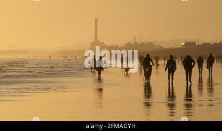 Brighton und Hove Beach bei Ebbe mit Blick nach Westen in Richtung Shoreham. Silhouetten von Menschen, die bei Sonnenuntergang am Sandstrand entlang wandern. East Sussex, England Stockfoto
