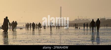 Brighton und Hove Beach bei Ebbe mit Blick nach Westen in Richtung Shoreham. Silhouetten von Menschen, die bei Sonnenuntergang am Sandstrand entlang wandern. East Sussex, England Stockfoto