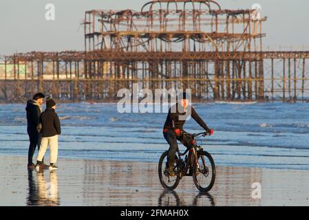 Strandgänger am Brighton Beach bei Ebbe, Spätnachmittag, Frühling. Brighton, Sussex, England. Radfahren auf dem Sand