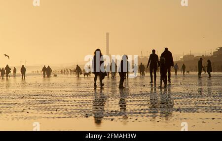 Brighton und Hove Beach bei Ebbe mit Blick nach Westen in Richtung Shoreham. Silhouetten von Menschen, die bei Sonnenuntergang am Sandstrand entlang wandern. East Sussex, England Stockfoto