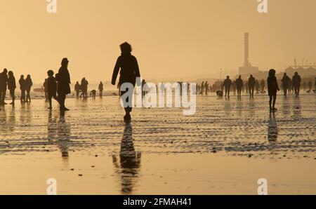 Brighton und Hove Beach bei Ebbe mit Blick nach Westen in Richtung Shoreham. Silhouetten von Menschen, die bei Sonnenuntergang am Sandstrand entlang wandern. East Sussex, England Stockfoto