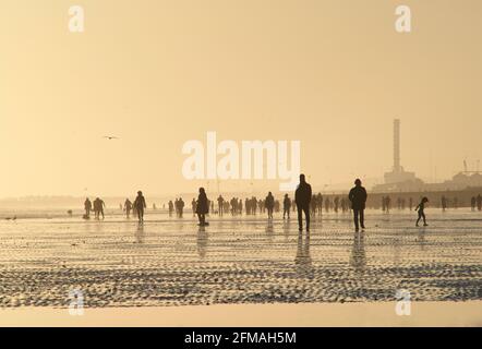 Brighton und Hove Beach bei Ebbe mit Blick nach Westen in Richtung Shoreham. Silhouetten von Menschen, die bei Sonnenuntergang am Sandstrand entlang wandern. East Sussex, England Stockfoto