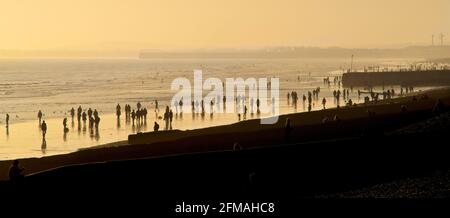 Brighton und Hove Beach bei Ebbe mit Blick nach Westen in Richtung Worthing. Silhouetten von Menschen, die bei Sonnenuntergang am Sandstrand entlang wandern. East Sussex, England Stockfoto