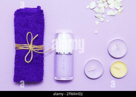 Duftkerzen, Handtuch, Lotion und Kieselsteine auf fliederfarbenem Hintergrund. Draufsicht, Kopierbereich, flach liegend. Spa- und Körperpflegekonzept. Stockfoto