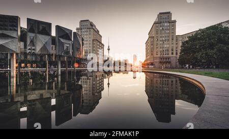 Spiegelung der Gebäude am Strausberger Platz im Wasser des Brunnens mit dem Fernsehturm im Hintergrund bei Sonnenuntergang. Stockfoto