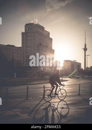 Radfahrer im Hintergrund bei Sonnenuntergang am Strausberger Platz mit dem Berliner Fernsehturm im Hintergrund. Stockfoto