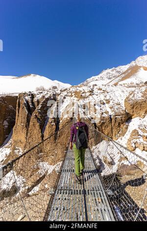 Junge Frau wandert über eine Hängebrücke nach Ghyakar in Upper Mustang, Nepal Stockfoto