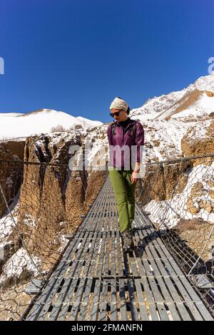 Junge Frau wandert über eine Hängebrücke nach Ghyakar in Upper Mustang, Nepal Stockfoto