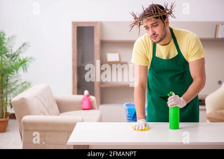 Junger männlicher Auftragnehmer, der auf dem Kopf einen stacheligen Kranz trägt und Hausarbeit leistet Stockfoto